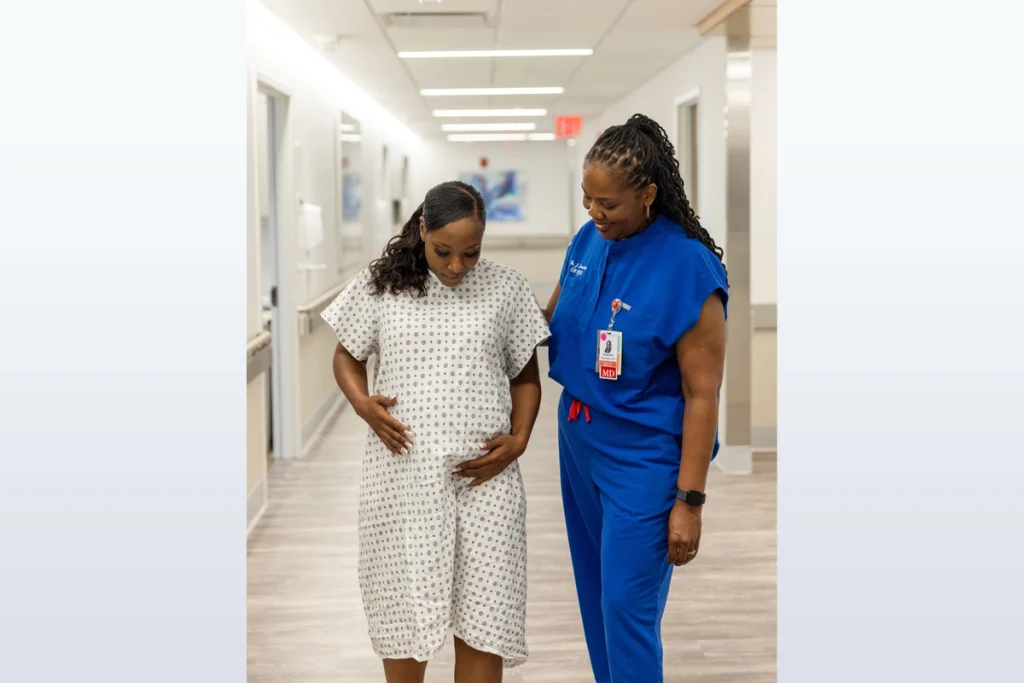 Doctor and pregnant patient walk together in maternity ward hallway.